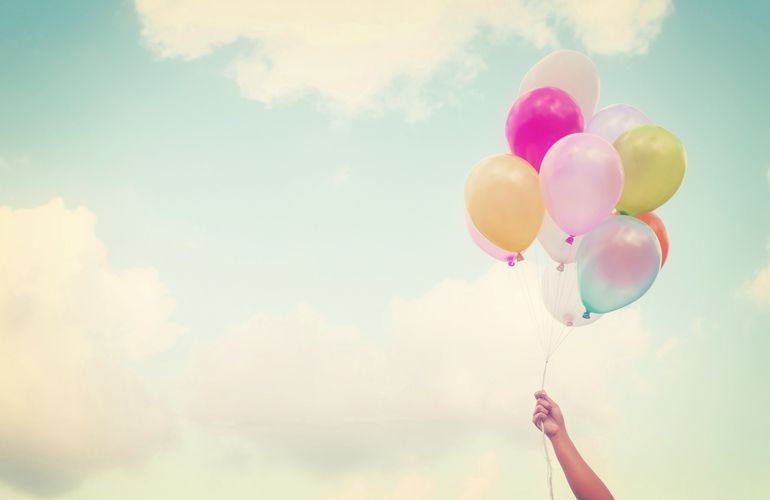 hand holding bundle of balloons against clouds in sky